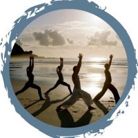 A picture of 4 people holding a yoga pose on the beach at sunrise